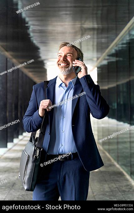 Cheerful mature businessman talking on mobile phone standing in corridor