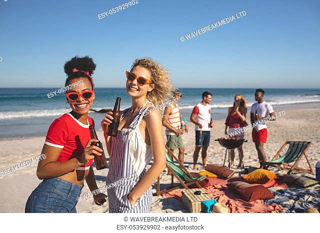Front view of two diverse friends have beer while diverse friends making a barbecue on the beach
