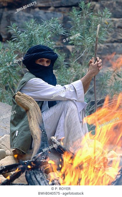 elder Touareg behind a camp fire, sitting on rocks, looking into flames, Algeria, Suedalgerien