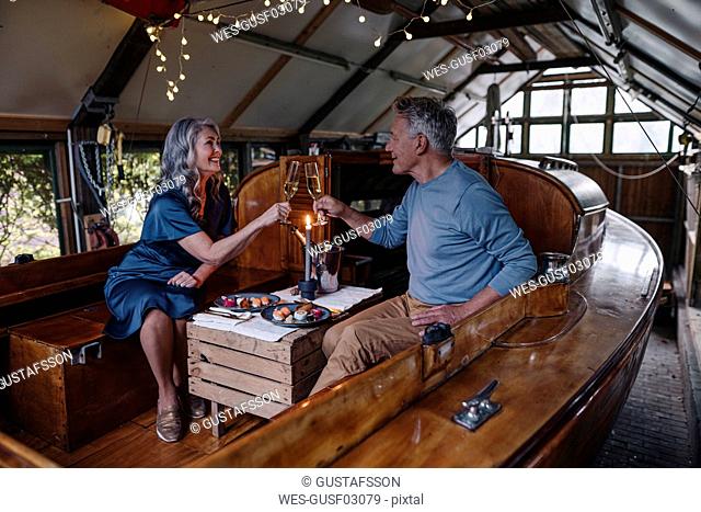 Senior couple having a candlelight dinner on a boat in boathouse clinking champagne glasses