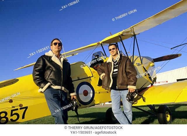 Two pilots with flying jackets near old British trainer biplane De Havilland DH 82a Tiger Moth used by the Royal Air Force