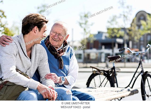 Happy senior man with adult grandson sitting on a bench