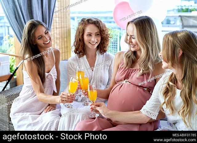 Smiling pregnant woman toasting cocktail glasses with friends