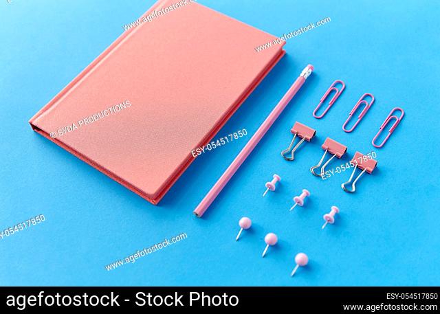 pink notebook, pins, clips and pencil on blue