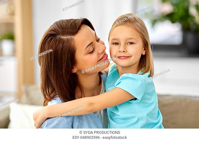 little daughter hugging her mother on sofa at home