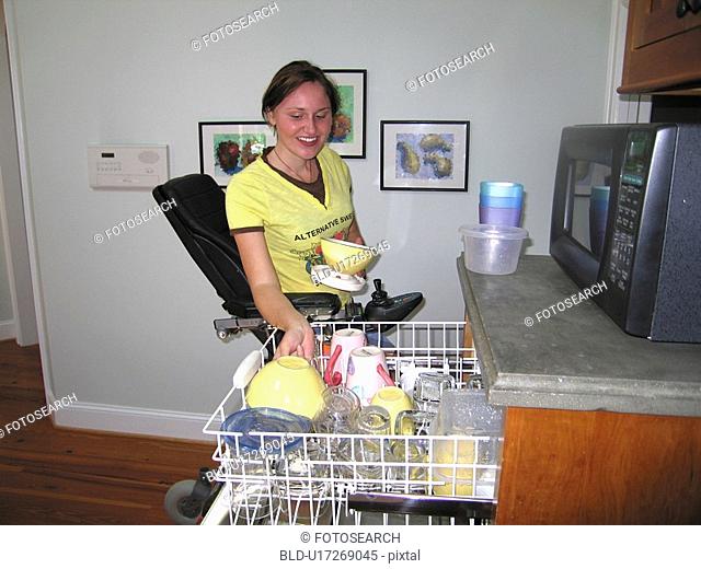 Young woman (wheelchair user) empties clean dishes from an accessible dishwasher