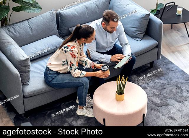 Businessman discussing over tablet computer with businesswoman on sofa