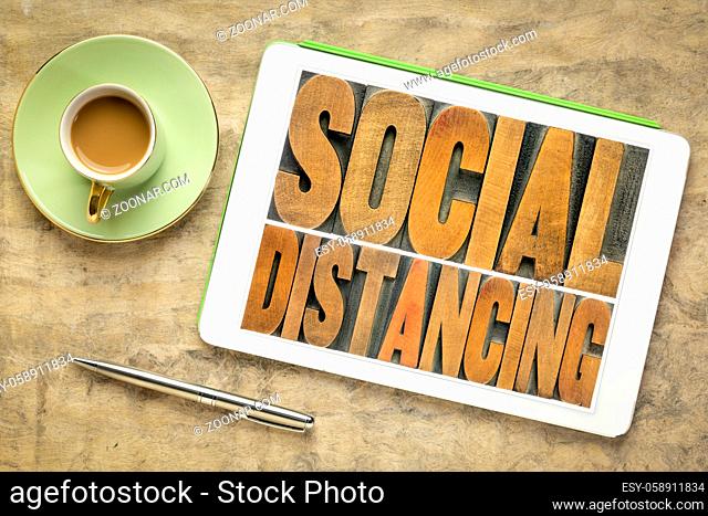 social distancing word abstract in vintage letterpress wood type on a digital tablet with coffee, protective measures during covid-19 corona virus pandemic