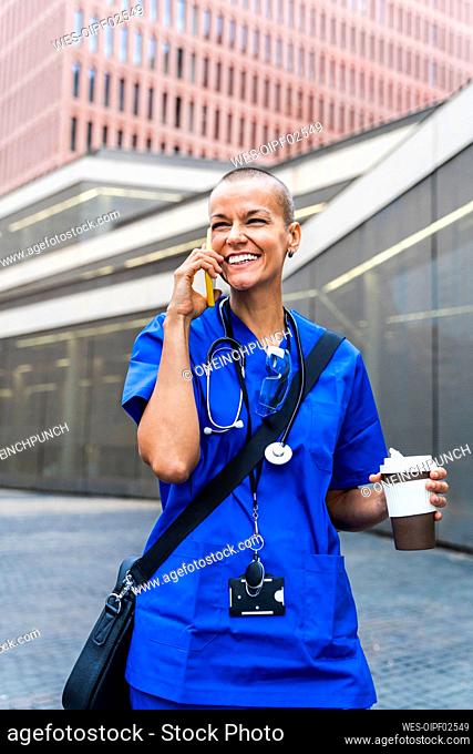 Happy mature nurse with disposable coffee cup talking on mobile phone