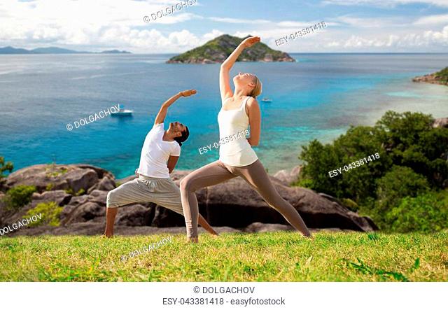 fitness, sport, people and healthy lifestyle concept - couple doing yoga in warrior pose over natural background and sea