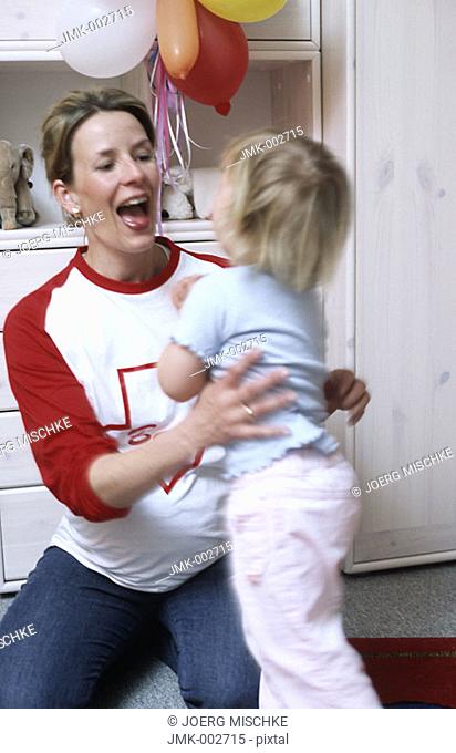 A young pregnant mother, woman, 25-30 30-35 35-40 years old, playing with her little daughter, 1-5 years old, in the nursery