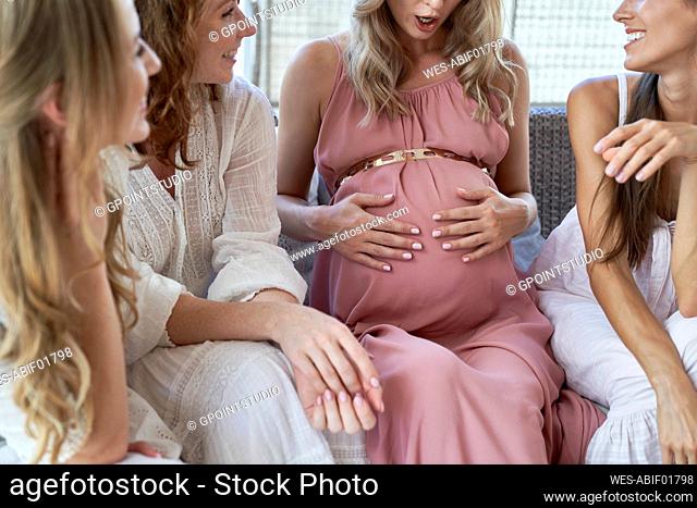 Surprised pregnant woman with hand on belly by friends at baby shower