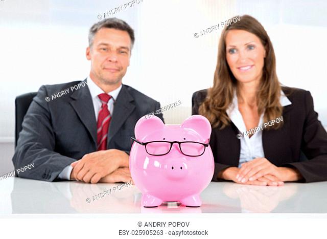 Two Happy Businesspeople Looking At Pink Piggybank On Desk