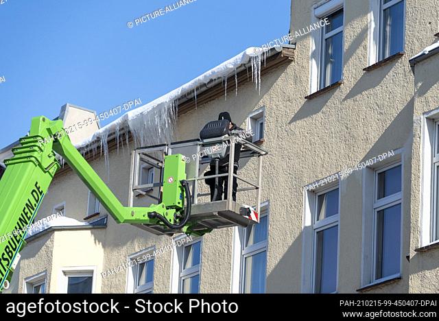 12 February 2021, Saxony-Anhalt, Magdeburg: A man drives a cherry picker to the roof of an apartment building to knock off icicles to protect pedestrians