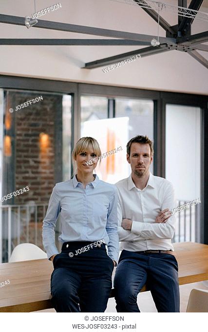 Successful businessman and woman standing in office, with arms crossed