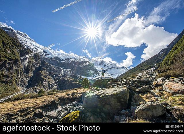 Mountaineer stands on rocks, view of Rob Roy Glacier, Sun Star, Mount Aspiring National Park, Otago, South Island, New Zealand, Oceania