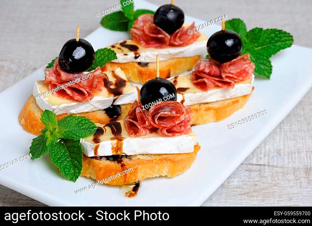Snack from a toasted slice of baguette with soft under a noble white mold Cheese Brie, salami, a berry of grapes with honey