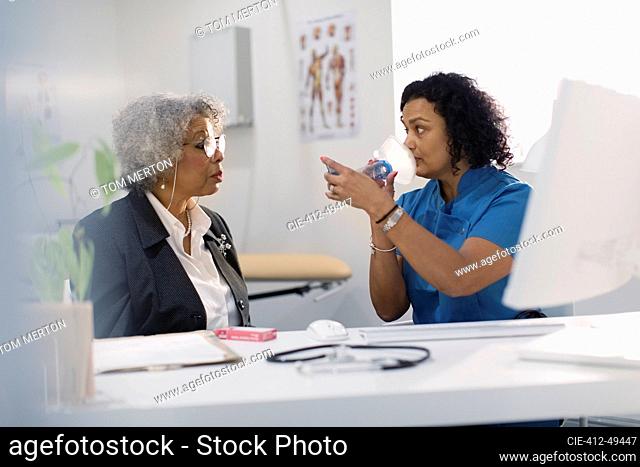 Female doctor teaching senior patient how to use inhaler in doctors office