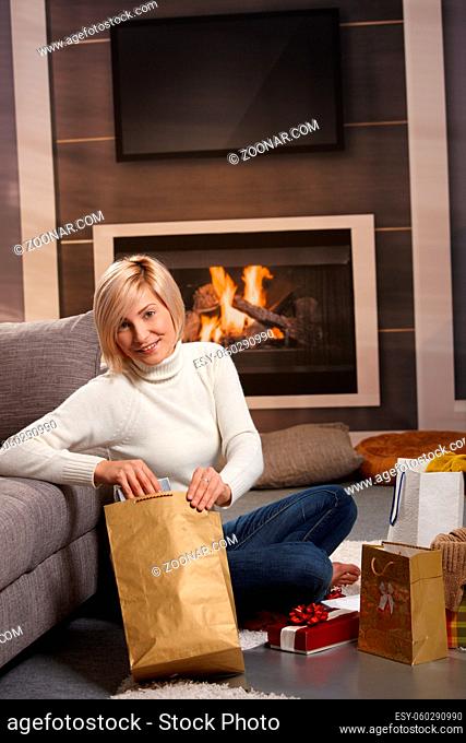 Woman siiting on floor at home in front of fireplace wrapping presents for Chrismas