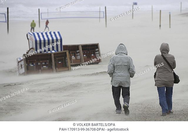 Sand is blown over the dunes by a stormy wind while to passerbys struggle to walk on the island Norderney, Germany, 13 September 2017