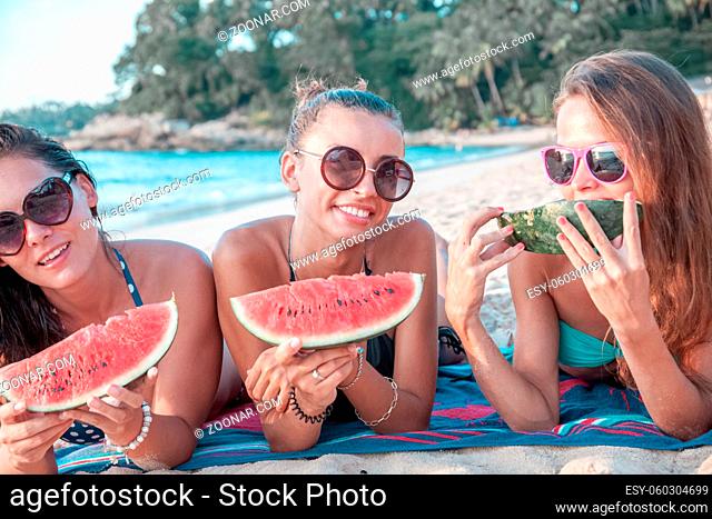 Happy smiling female friends eating watermelon on beach
