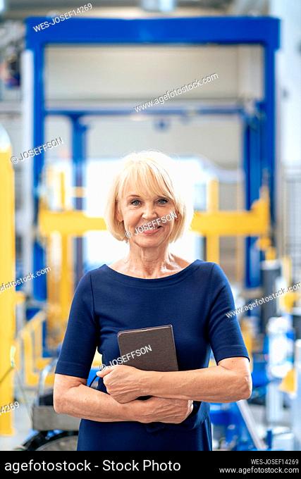 Happy businesswoman holding tablet computer standing in industry