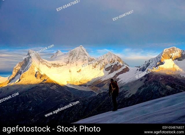 Horizontal view of a male mountain climber on Nevado Pisco glacier at sunrise with the four peaks of Nevado Huandoy in the background
