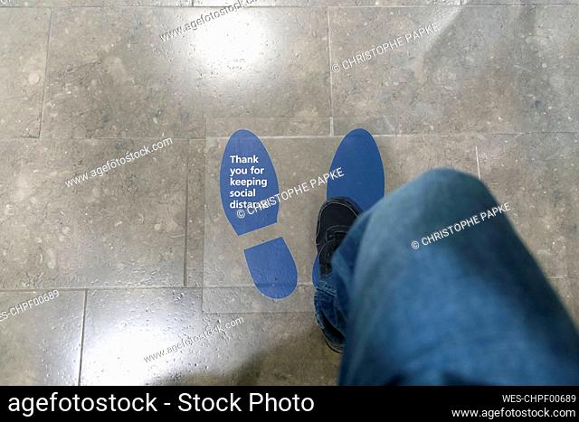 Woman stepping on floor sticker written Thank You For Keeping Social Distance on it