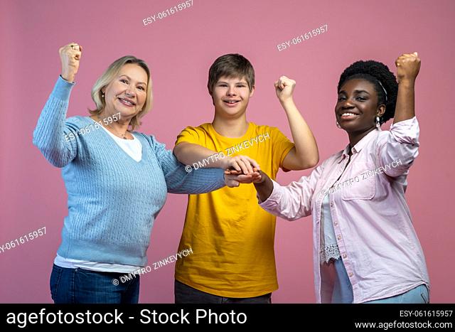 Team. Guy with down syndrome and two women standing touching with palms smiling at camera with raised fists