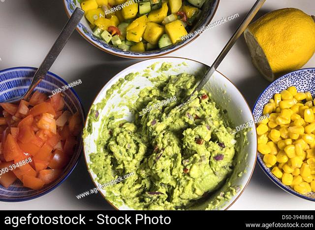 Bowls in a kitchen filled with guacamole, corn, tomatoes, mango and cucumber
