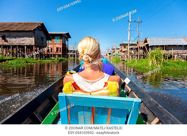 Rear view of female Caucasian tourist traveling by colorful traditional wooden boat on Inle lake, Burma, Myanmar