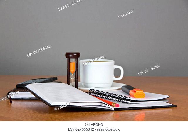 Open notepad, marker pencil, the calculator, hourglasses and a cup of coffee on a table