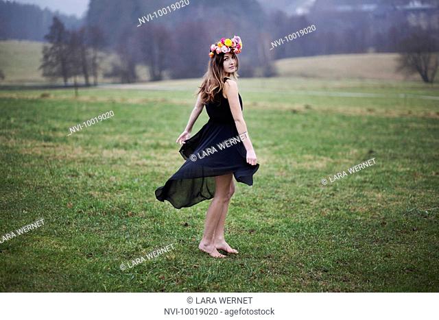 Young woman with flower wreath dancing on a meadow