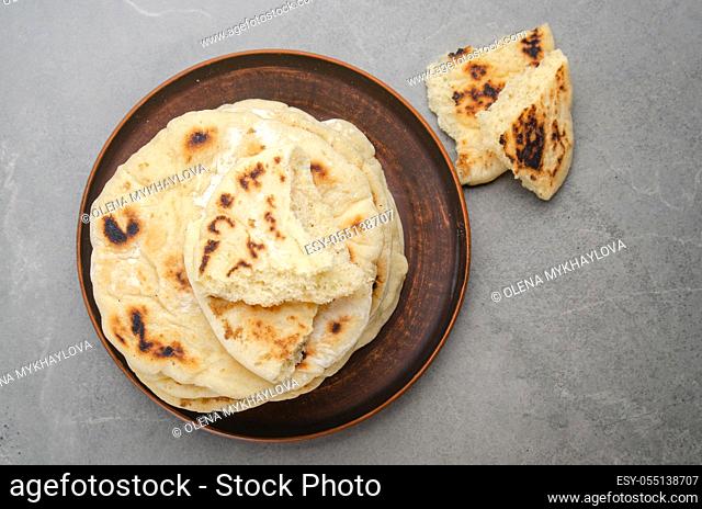 Flat lay view at homemade tasty traditional Pita bread stacked in clay dish on stone kitchen table