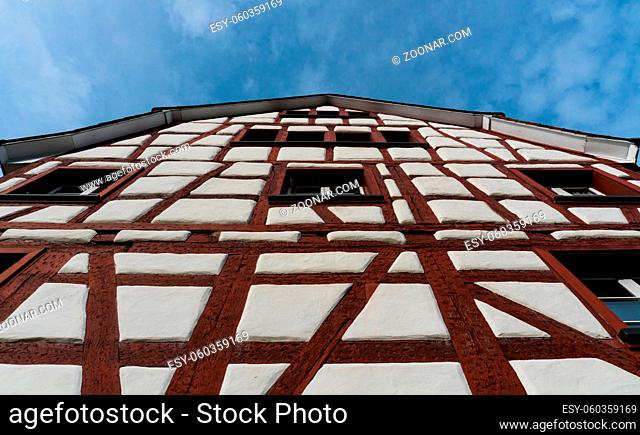 close up frog perspective view of a half-timbered truss house with white walls and red wooden beams under a blue sky in the picturesque village of Neunkirch in...
