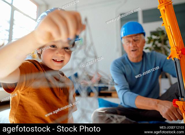 Boy examining electricity pylon model by grandfather at home