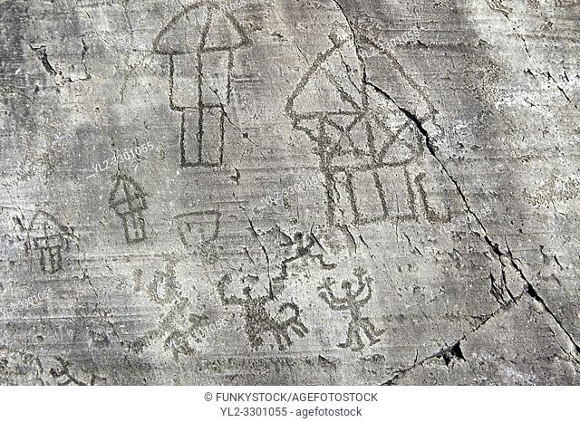 Petroglyph, rock carving, of a village with houses on stilts and a ceremony. Carved by the ancient Camunni people in the iron age between 1000-1200 BC