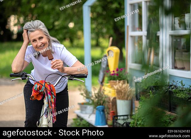 Happy woman. Cheerful woman on a bike eating ice-cream and looking happy