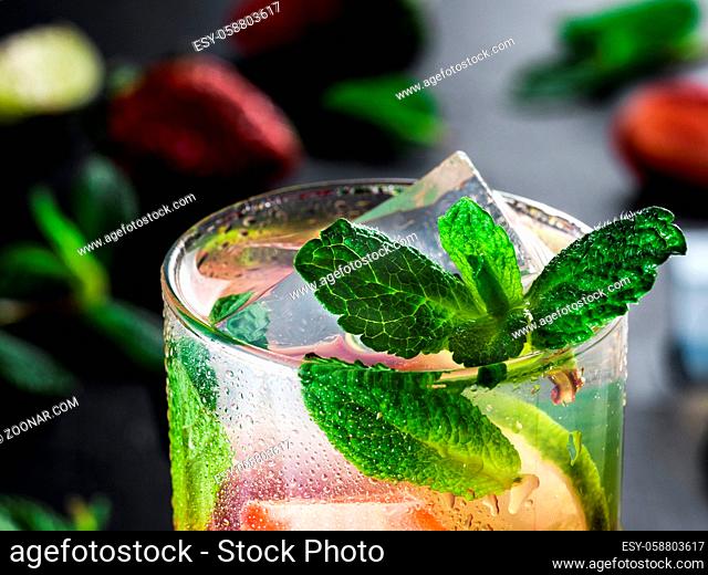 fresh lemonade with strawberry, lime and mint on dark stone background. Cold summer strawberry drink with mint and ice. Strawberry mojito in glass and...