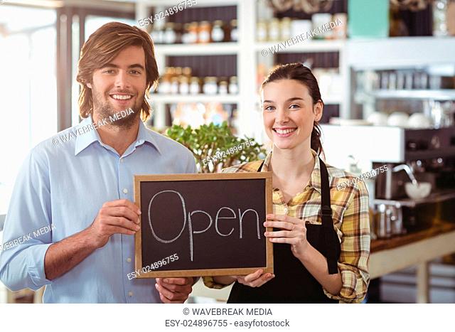 Portrait of man and waitress holding chalkboard with open sign