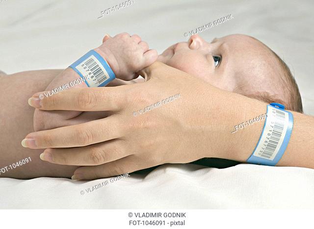 A baby holding her mother's thumb, both wearing hospital ID bracelets
