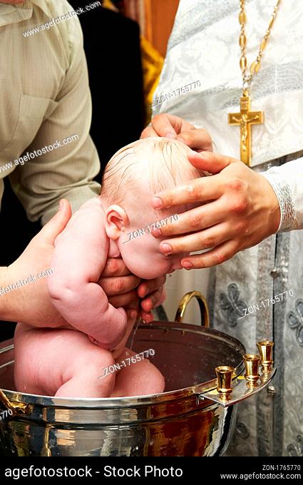 Newborn baby baptism by water in font with hands of priest