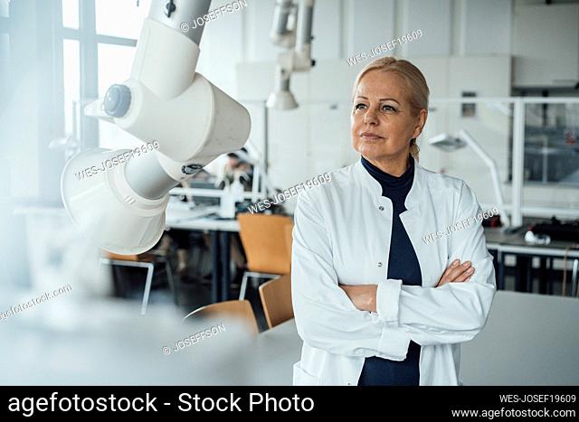 Thoughtful senior scientist standing with arms crossed in laboratory