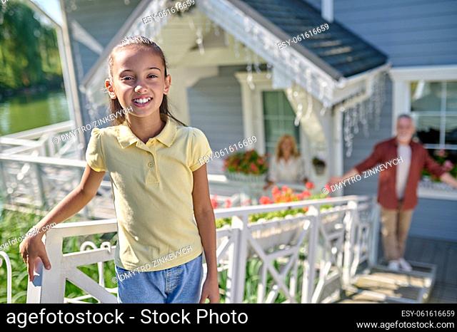 Happy girl. Cute girl standing near the house and smiling, dad looking at her