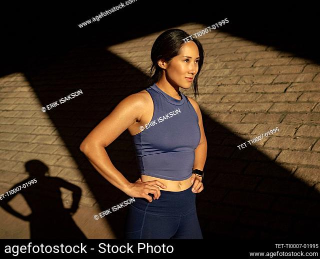 Woman in sports clothing near brick wall in sunlight