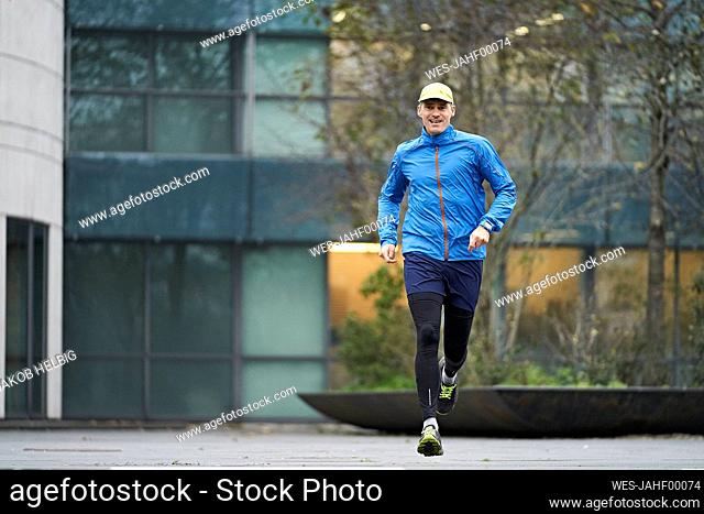 Mature man jogging wearing cap against building