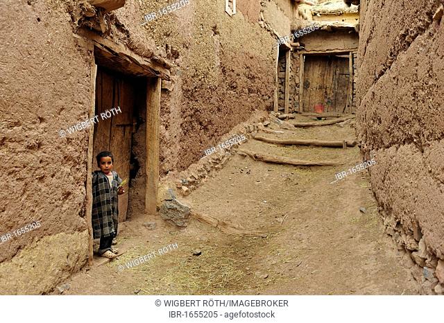Little Berber boy standing in front of a door in a narrow alleyway of an adobe village, Kelaa M'gouna, High Atlas mountains, Morocco, Africa