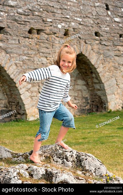 Niedliches kleines Mädchen posiert barfuß vor der Stadtmauer von Visby, Insel Gotalnd, Schweden, für den Fotografen und hat viel Freude dabei