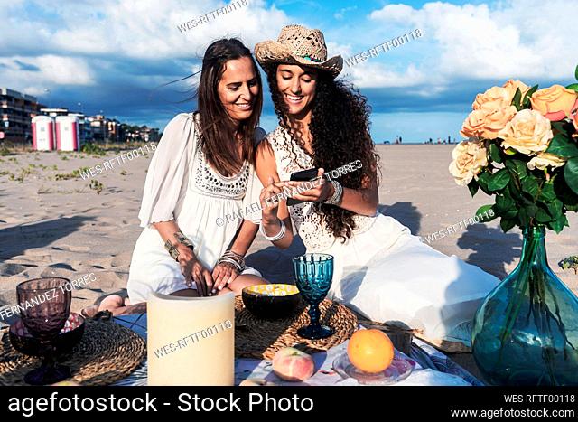 Smiling teenage girl sharing mobile phone with mature woman on beach