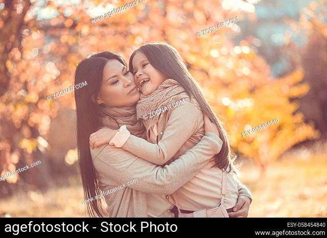 Half length image of brunette woman holding her kid. Being in autumn garden